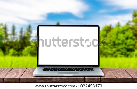 Modern laptop with empty white screen on wooden table against blurred landscape