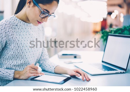 Concentrated female administrative signing online documentation via digital tablet and pen organizing office work at desktop,woman designer drawing sketch on modern gadgets synchronized with netbook