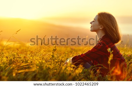 Woman sits with her back in the field and admires the sunset in the mountains