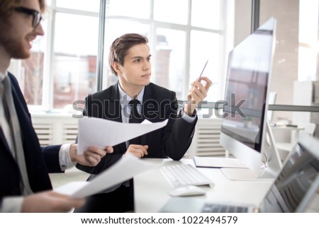 Young confident analyst pointing at monitor display while making presentation of financial or sales rate online