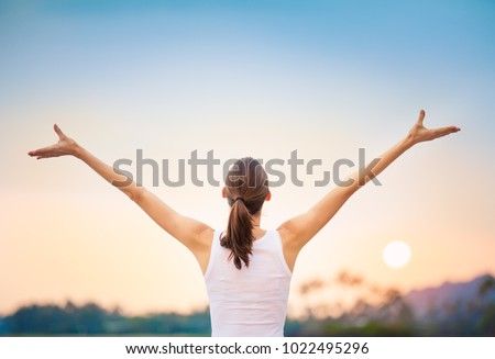 Young woman raising her arms up against the sunset feeling free.  Happiness and joy concept.  Royalty-Free Stock Photo #1022495296