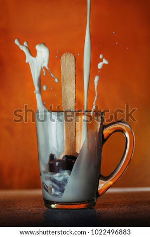 A sweet dessert chocolate-dipped spoon in a glass cup with hot flowing milk on orange background; selected focus
