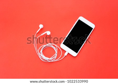 Smartphone with Blank Screen Connects to Earphones with Spiral Cable on Red Background Top View  Royalty-Free Stock Photo #1022533990