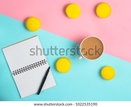 Notebook with a pen, a cup of coffee and yellow macaroons on a pastel colored background. Trend of minimalism. Top view. Flat lay.