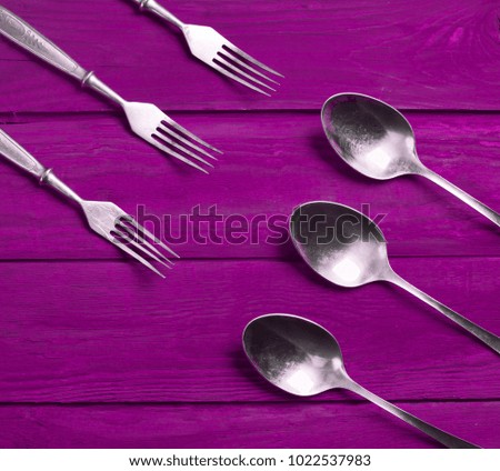 A group of spoons and forks on a colored wooden background.
