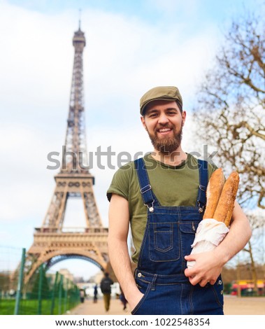 Handsome smiling bearded man holding baguette in hands over Eiffel Tower background