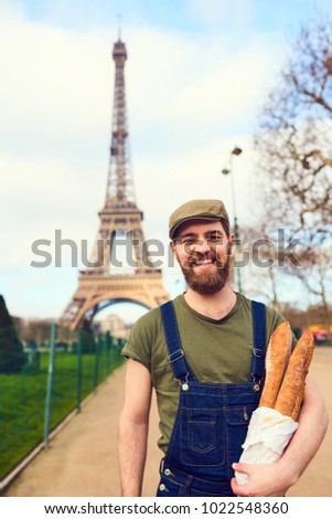 Handsome smiling bearded man holding baguette in hands over Eiffel Tower background