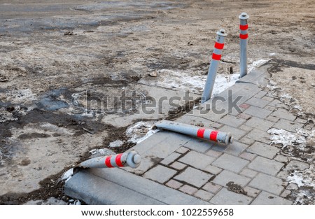 Gray broken bollards with red stripes at the parking zone