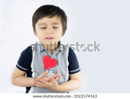 Adorable kid boy holding white camera model with red paper in heart shape and looking at camera with smiling face isolated on white background, Love or Mother day concept
