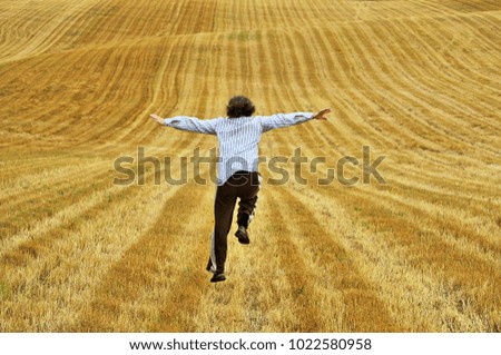 Man is running on a yellow field as if he wants to fly