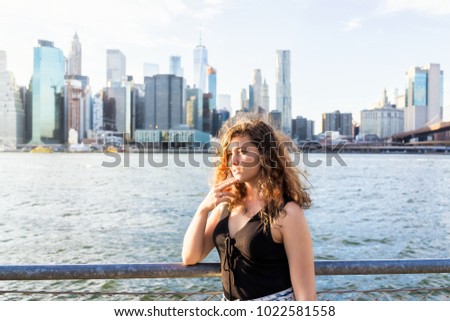 Back of young woman outside outdoors in NYC New York City Brooklyn Bridge Park by east river, railing, looking at view of cityscape skyline