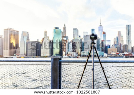 Camera, tripod set up outside outdoors in NYC New York City Brooklyn Bridge Park by east river, railing, taking pictures of cityscape skyline during sunset