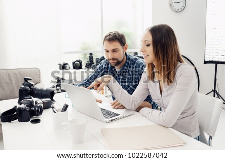 Photographer and designer in a creative agency, they are sitting at desk and working together with a laptop