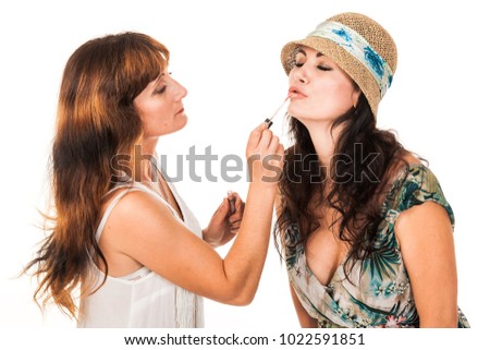 Two women. One another does the make-up. She paints her lips, and face. Smile, twisted. Isolated photo on the white background. You can use cosmetics advertising, lipsticks, makeup basics