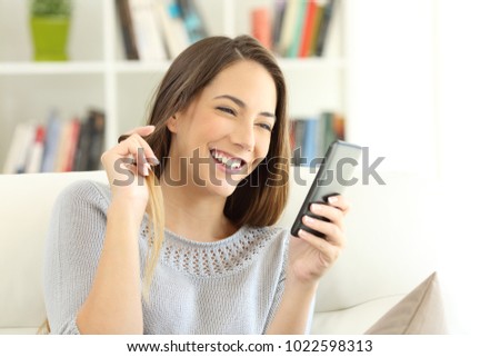 Girl flirting on line with a smart phone sitting on a couch in the living room at home