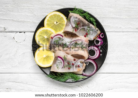 Herring fillet with salt, pepper, herbs, onion and lemon on black plate on white background. top view. healthy food Royalty-Free Stock Photo #1022606200