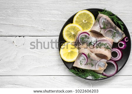 marinated herring fillet with pepper, herbs, onion and lemon on black plate on white background. top view with copy space. healthy food Royalty-Free Stock Photo #1022606203