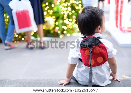 little boy toddler is sitting in shopping mall he wearing kid Strapped on the leash.