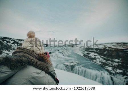 Young woman with hat taking pictures in Gullfoss waterfall in wintertime