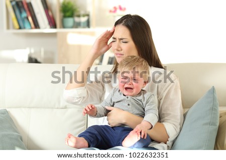 Mother suffering and baby crying desperately sitting on a couch in the living room at home Royalty-Free Stock Photo #1022632351