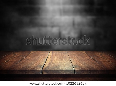 Old wood table with blurred concrete block wall in dark room background. Royalty-Free Stock Photo #1022632657