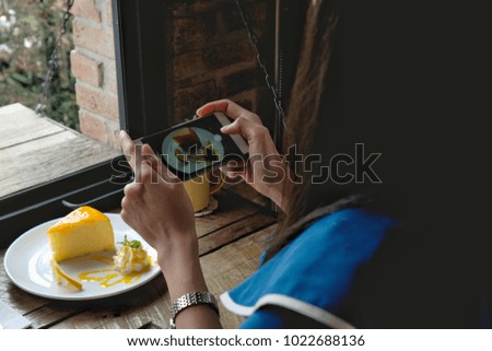 Asian girl taking a photo before enjoy and eat an orange cake set on the wooden table.