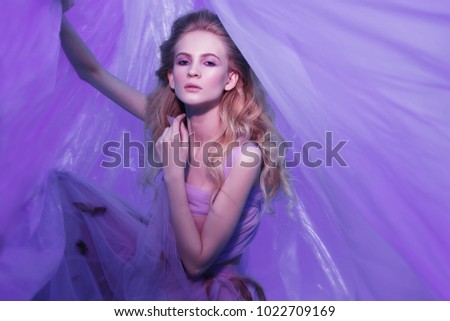 Fashion portrait of young beautiful woman in fluffy violet dress. Blond curly hair, makeup, dress with feathers, soft colors, art photo