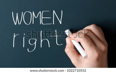 Green chalkboard with hand holding white chalk. WOMEN RIGHTS handwriting.