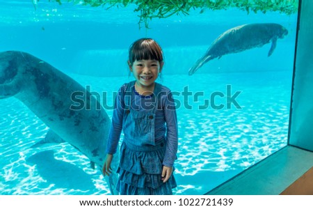Asian little girl happy in zoo with manatees in glass tank. Little girl on vacation in summer.