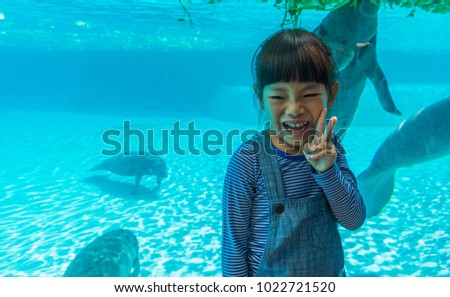 4 years old, little Asian girl in front of manatee's glass tank. Little girl on vacation in summer. Smiling face of little girl. Space for text.