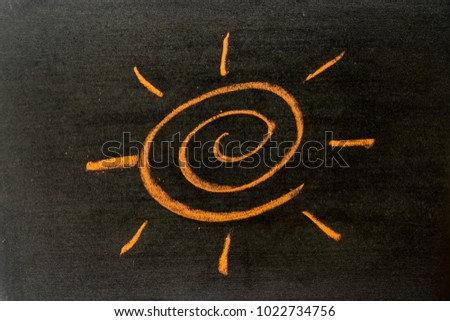 Orange color chalk hand drawing as sun with light ray shape on black board background