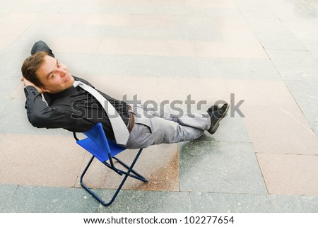 Image of the businessman sitting andrelaxing in the empty street. Focus is made on top of the background marbled tile in the street.