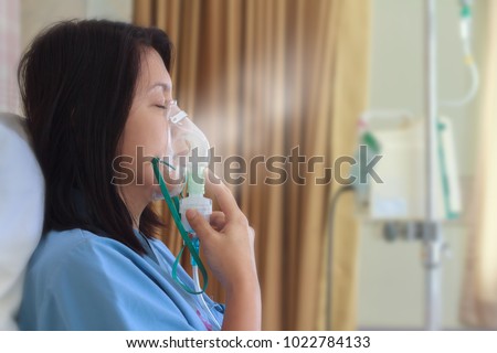 Sick beautiful female in blue cloth hold nasal mask with respiratory problem in hospital room. Asian woman patient inhalation therapy by the mask of inhaler with soft stream smoke from bronchodilator. Royalty-Free Stock Photo #1022784133