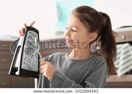 Cute little girl playing music with grater and spoon in kitchen