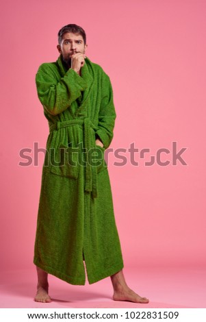 a man in a green robe yawns full length on a pink background                               