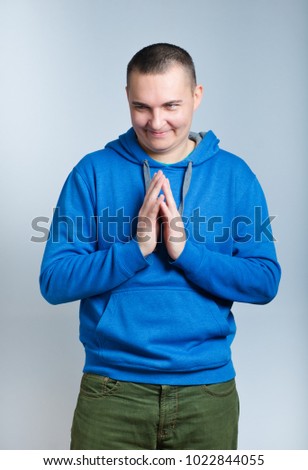 portrait of a cunning man, came up with something interesting, dressed in a blue hoodie, isolated on a gray background