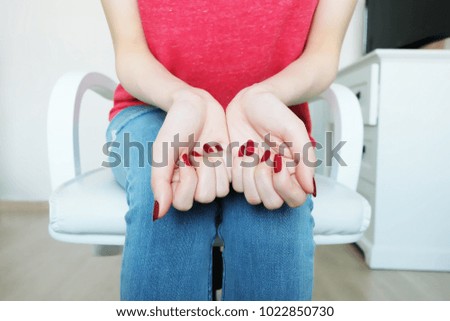 Close Up Red Nails Manicure Cosmetics. Beautiful Woman with Red Nail Polish and Red Shirt Sitting on a White Chair Background Great for Any Use.