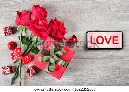 Happy Valentine's Day Concept with red roses, gift boxes, smartphone and love word on mobile screen