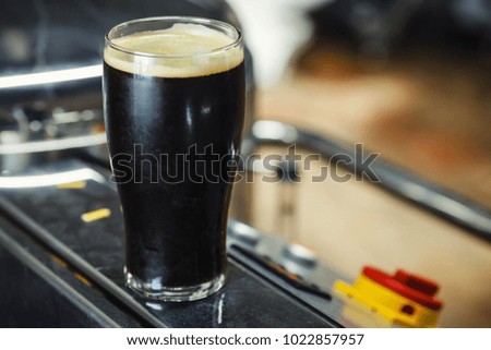 Pint glass of dark stout beer standing on brewing equipment in an operating brewery