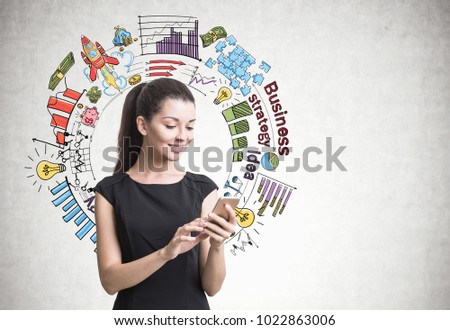 Beautiful young businesswoman in a black dress looking at her smartphone screen. A concrete wall background with business planning icons. Mock up