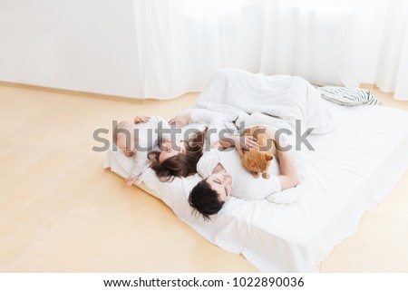 Family is happiness. Positive mom and charming dad playing with red cat and small restless baby lying on bed in the white interior. Lifestyle real picture