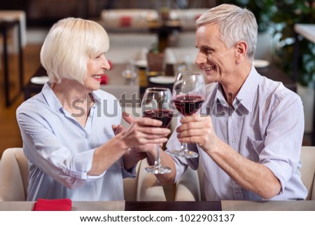Great wine. Joyful merry mature couple carrying glasses of wine while talking and posing in profile