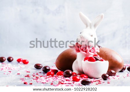 Porcelain Easter bunny with brown and red chocolate eggs and colorful sugar, gray background, selective focus