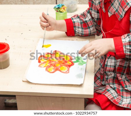 A girl draws a drawing with paints on a sheet