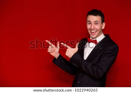 Young Stylish man in suit pointing finger and looking in camera. Photo for business projects, product presentation. Image with copy space isolated on red