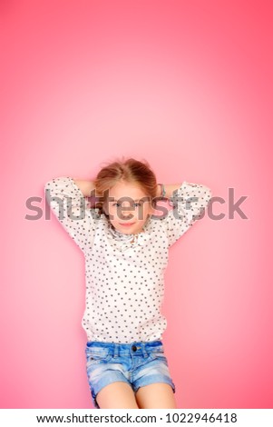 Happy childhood. Cute eight year old girl wearing summer jeans shorts and blouse lying on a pink floor. Studio shot. 