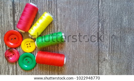 Photo of sewing accessories red,yellow and green color (threads, pins and needle) on a wooden background.Tools for handwork.Top view