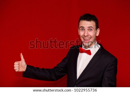 Half body photo of Young Stylish man in suit giving thumb up. Happy man with arm bent at the elbow and thumb up fun sign isolated on red background. Positive, successful, approve, motivation gesture