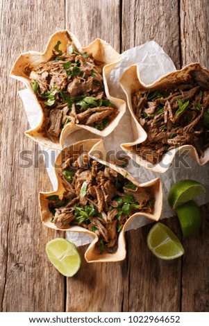 Mexican barbacoa with beef, lime and greens close-up on paper on table. Vertical top view from above
