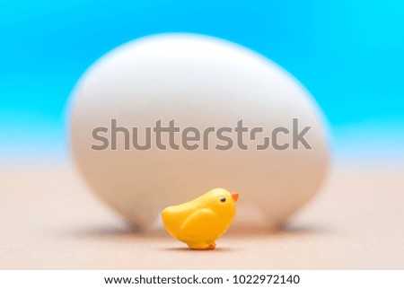Little toy yellow chick  near the big white egg on a blue background